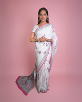Woman wearing a white saree with pink and black patterns on a pink background